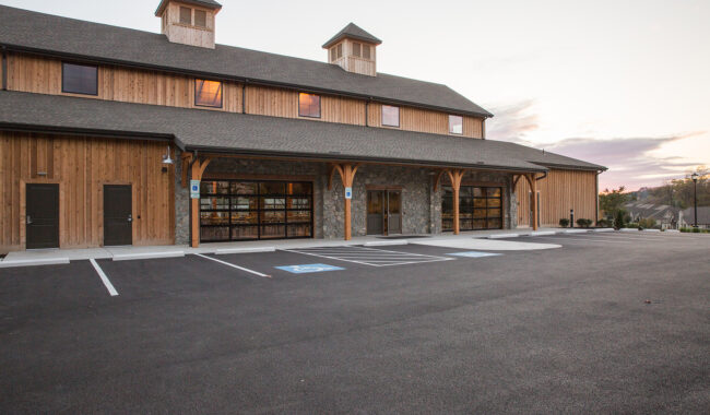 A large wooden building with stone accents, overhanging roof, and cupolas sits next to an empty, paved parking lot with designated accessible parking spaces at sunset.