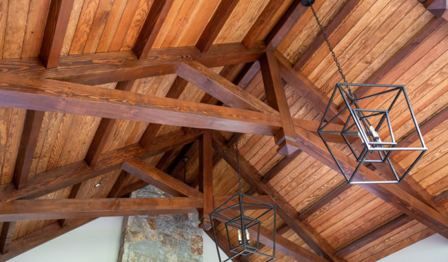 Vaulted wooden ceiling with exposed beams and two modern geometric pendant light fixtures. Part of a stone and brick fireplace is visible at the bottom of the image.