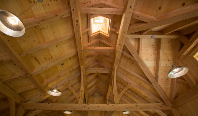 A wooden vaulted ceiling with exposed beams, illuminated by hanging industrial-style pendant lights and natural light from a small skylight window.