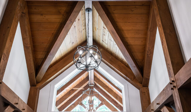 Wooden vaulted ceiling with exposed beams, two modern geometric pendant lights, and large triangular windows letting in natural light.