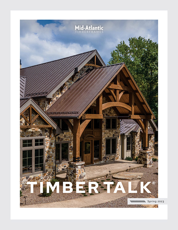 Cover of Timber Talk Spring 2023 magazine featuring a large stone and timber-framed house with a metal roof, surrounded by trees and blue sky, published by Mid-Atlantic Timberframes.